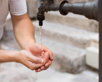 Close-up of hands catching water from an outdoor well faucet, showing reliable filtration for well water systems in Texas homes
