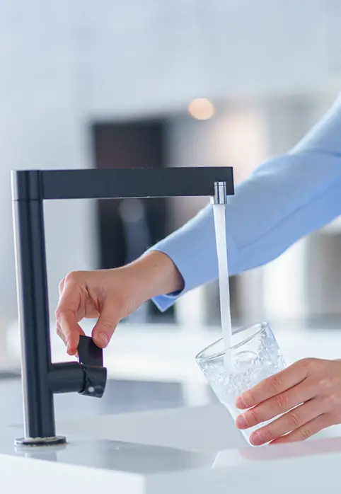 Person filling glass with filtered tap water from modern kitchen faucet